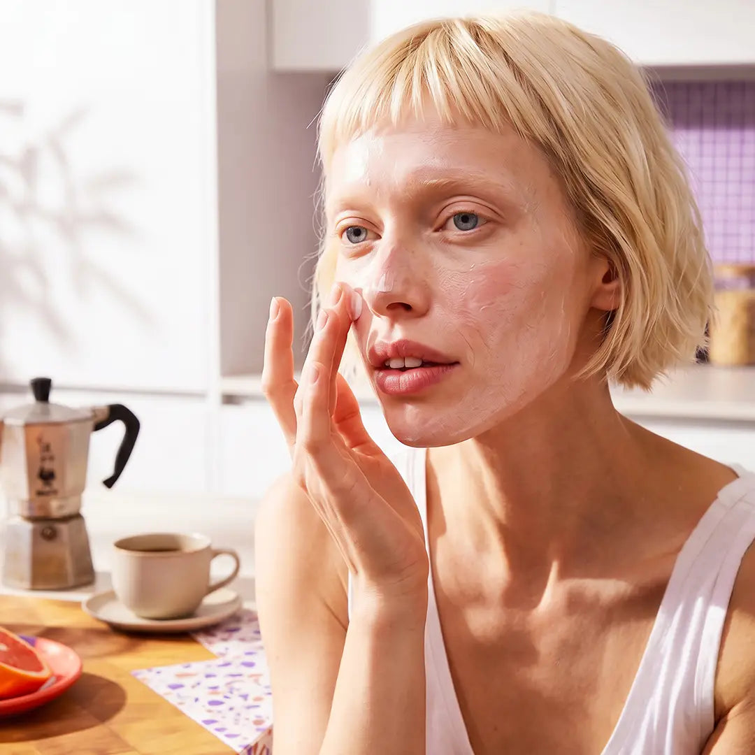 Model applying Yelf Spot Off Anti-Redness Cream in a soft morning kitchen setting with warm sunlight, visible skincare texture and relaxed everyday atmosphere.