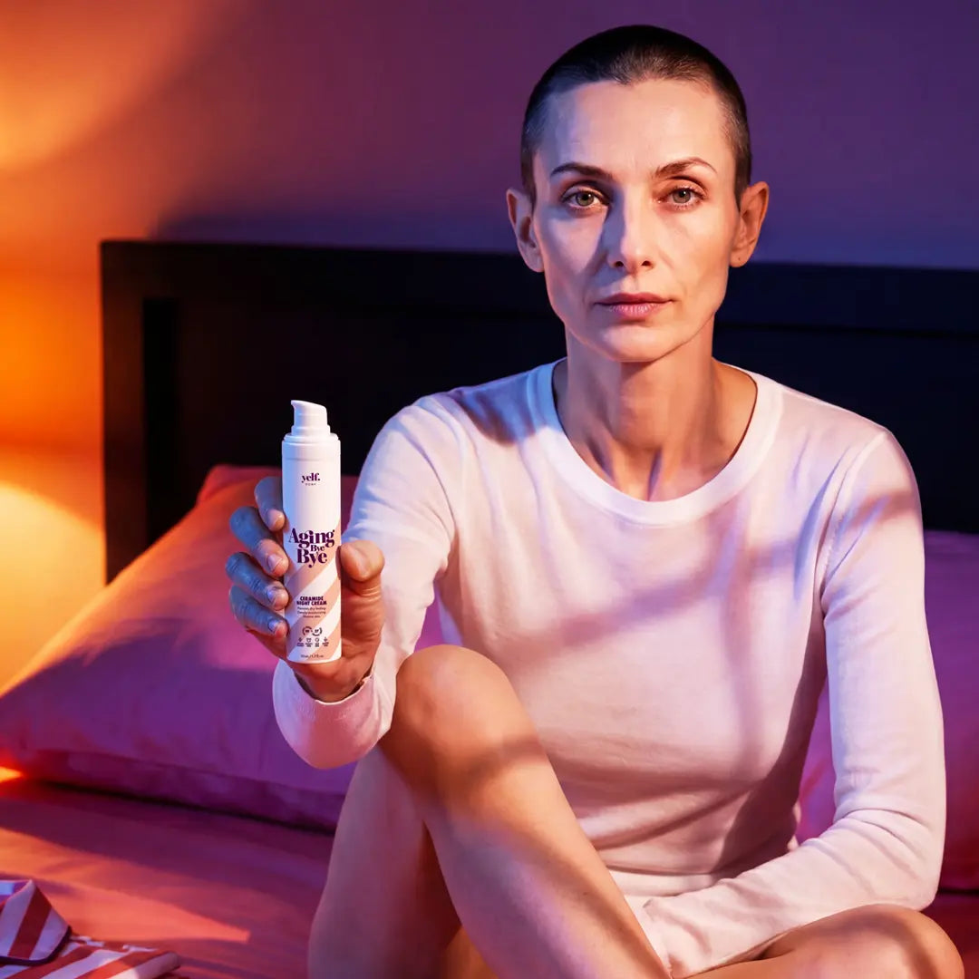 Editorial night skincare portrait of a woman holding Yelf Aging Bye Bye Ceramide Night Cream while sitting on a bed in moody pink and blue lighting.