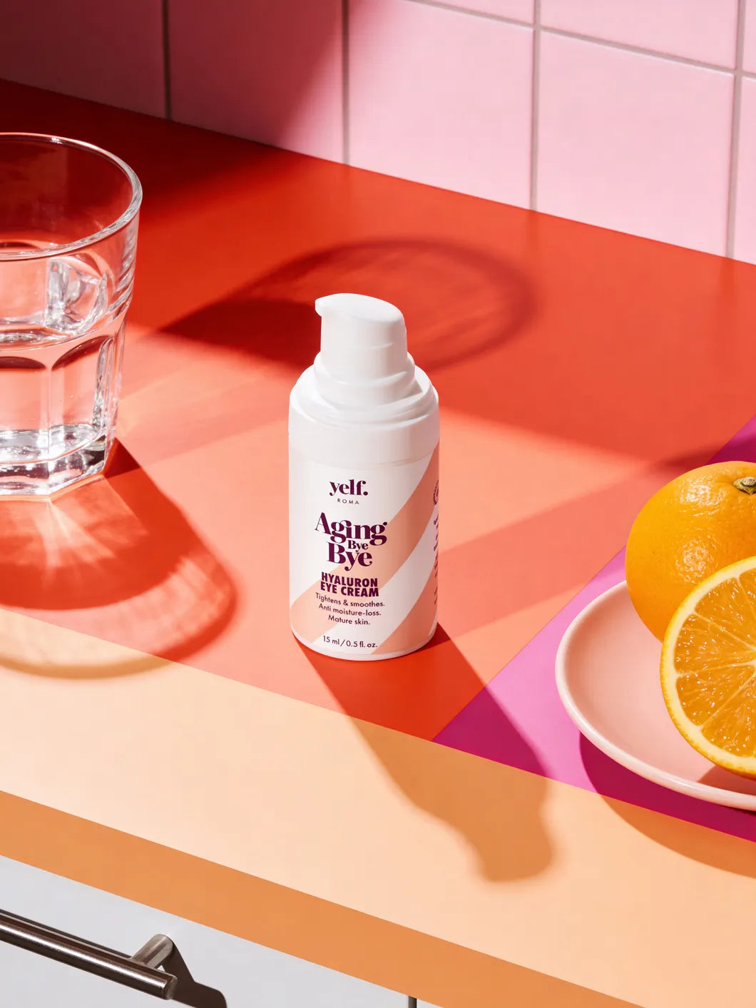 Yelf Aging Bye Bye Hyaluron Eye Cream on a colorful kitchen counter with a glass of water and fresh orange in bold morning light
