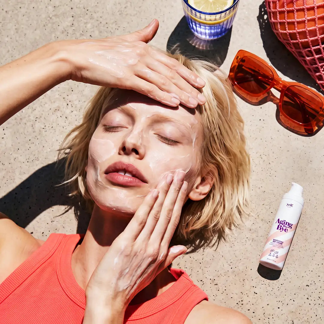 Model applying Yelf Aging Bye Bye Nourishing Day Cream in a sunlit summer lifestyle scene with bold shadows, sunglasses and fresh skincare texture on the skin.