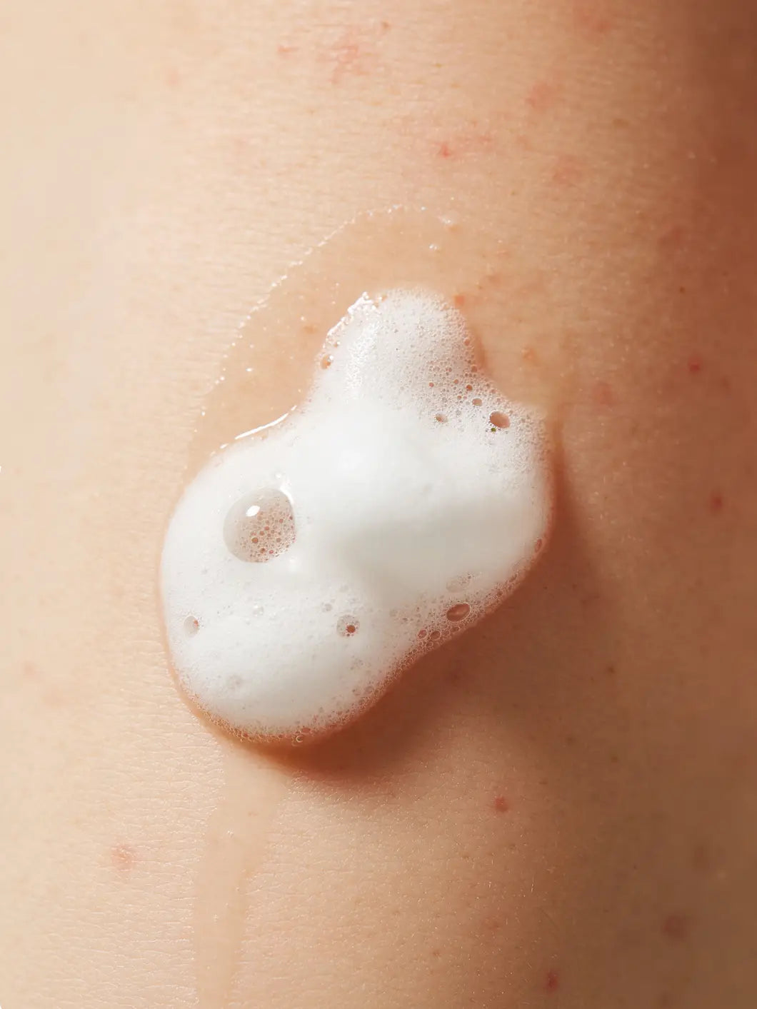 Airy cleansing foam texture with fine bubbles on skin, showing lightweight gentle facial cleansing