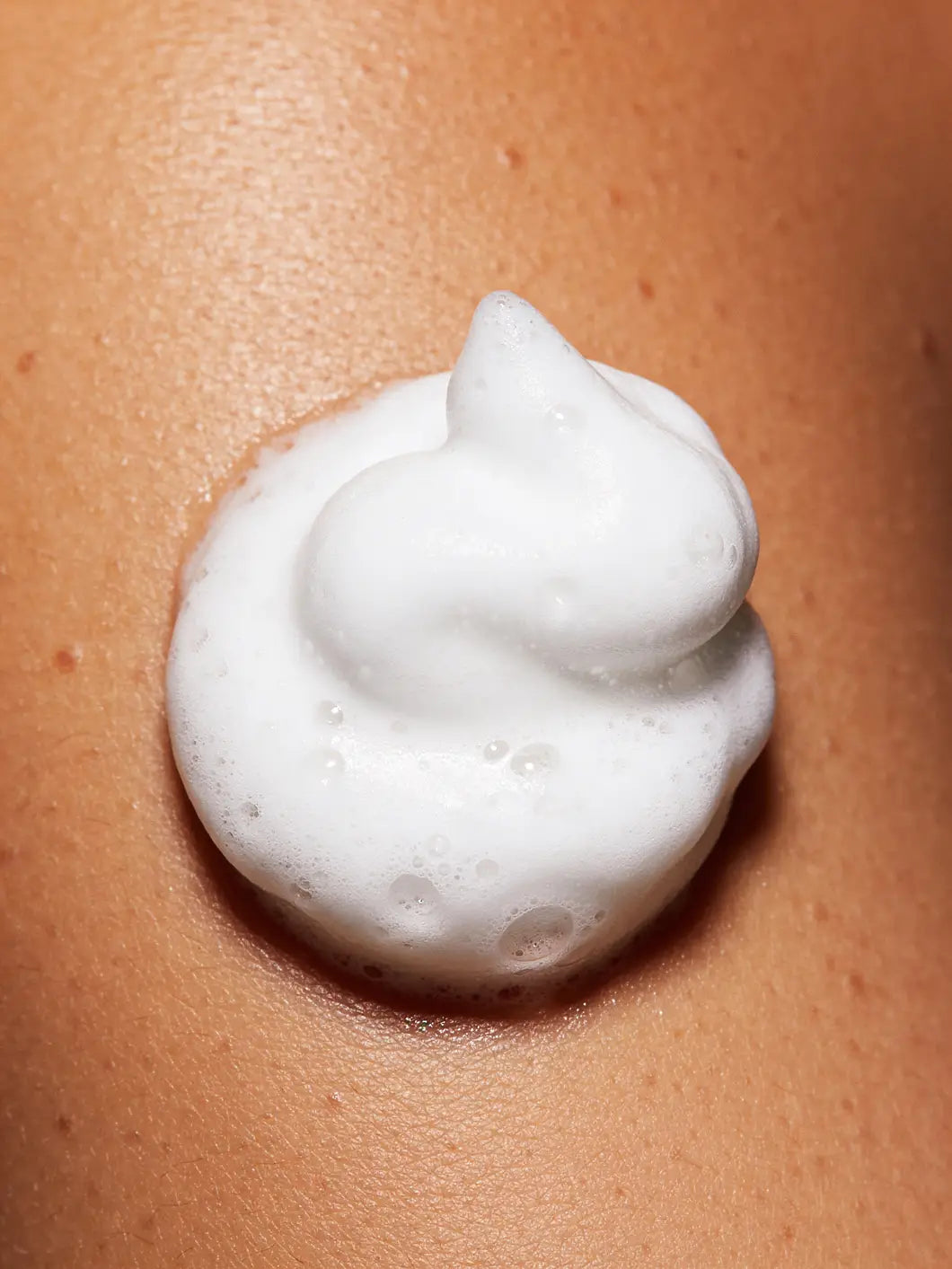 Dense purifying mousse foam with structured bubbles on skin, showing rich airy texture for deep facial cleansing