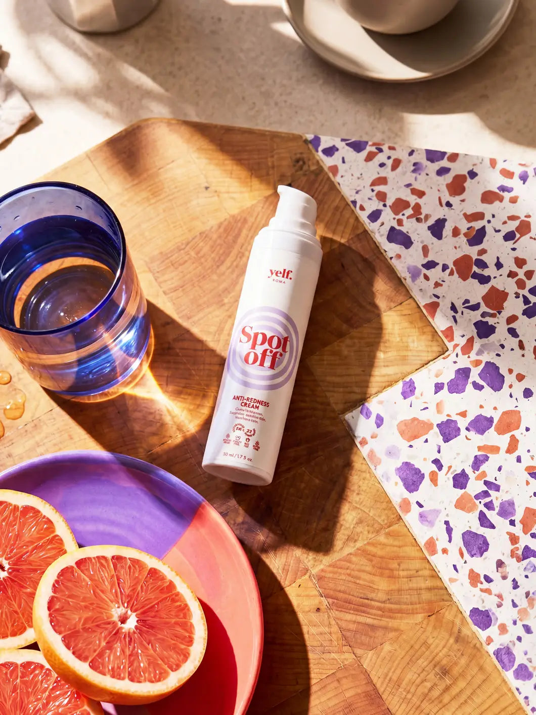 Yelf Spot Off Anti-Redness Cream on a wooden surface with grapefruit, glass of water and terrazzo elements in a warm, sunlit scene