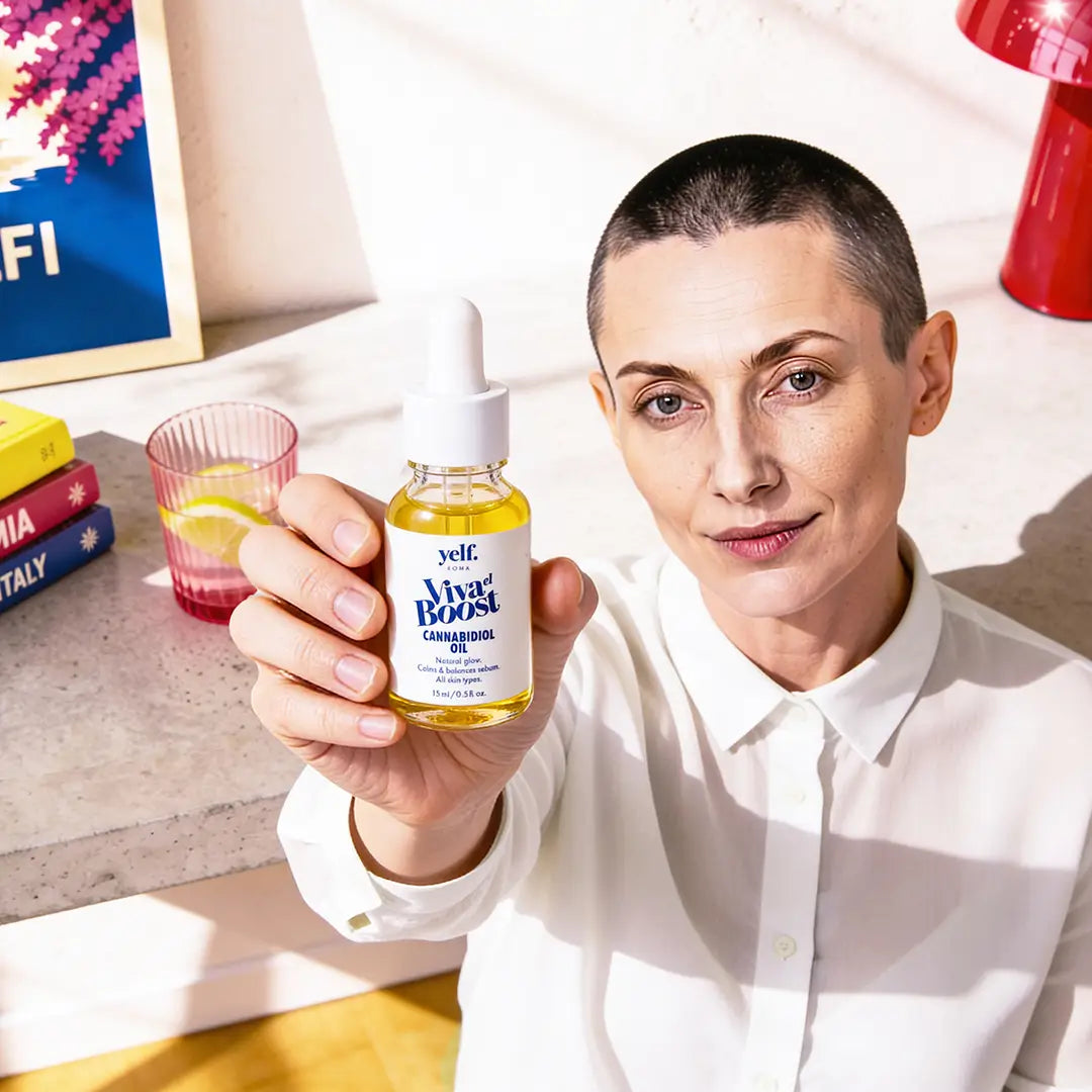 Woman holding Yelf Viva el Boost Cannabidiol Oil in a bright editorial home interior with warm sunlight, colorful design objects and relaxed skincare lifestyle atmosphere.